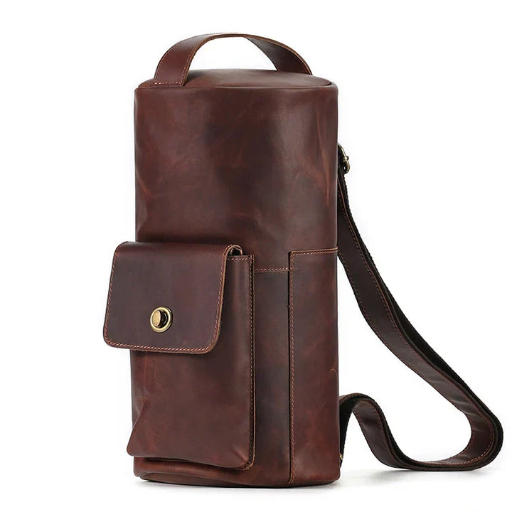 Borsa a tracolla in pelle marrone, design cilindrico, con tasca frontale e chiusura a bottone. Accessorio moda elegante e funzionale per uomo e donna.