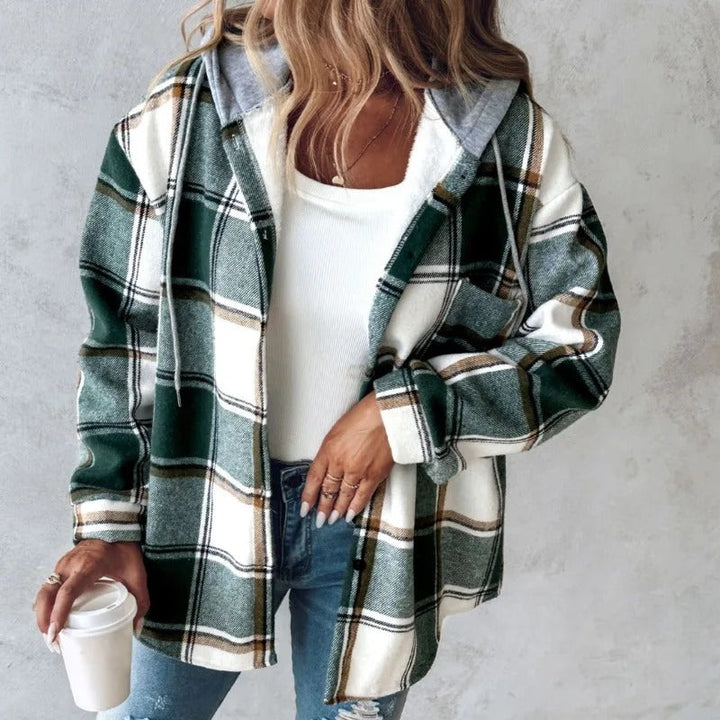 Donna con camicia a quadri verde e bianca, cappuccio grigio, jeans strappati, tiene una tazza di caffè. Moda casual autunnale.