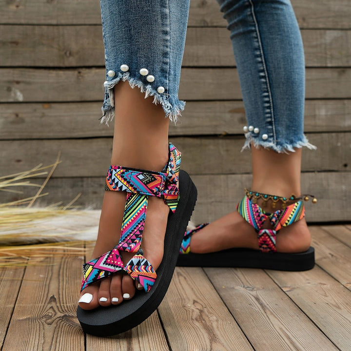 Sandali estivi donna con cinturini multicolore, suola nera, indossati con jeans strappati e perle. Scarpe moda casual, comode e trendy.