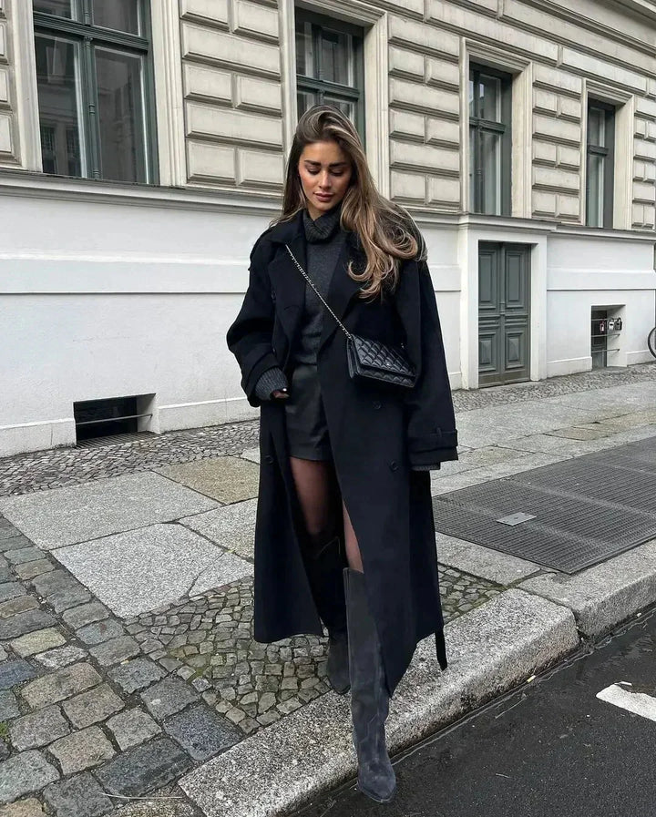 Manteau long noir femme en laine avec ceinture et larges revers pour une silhouette ajustée.