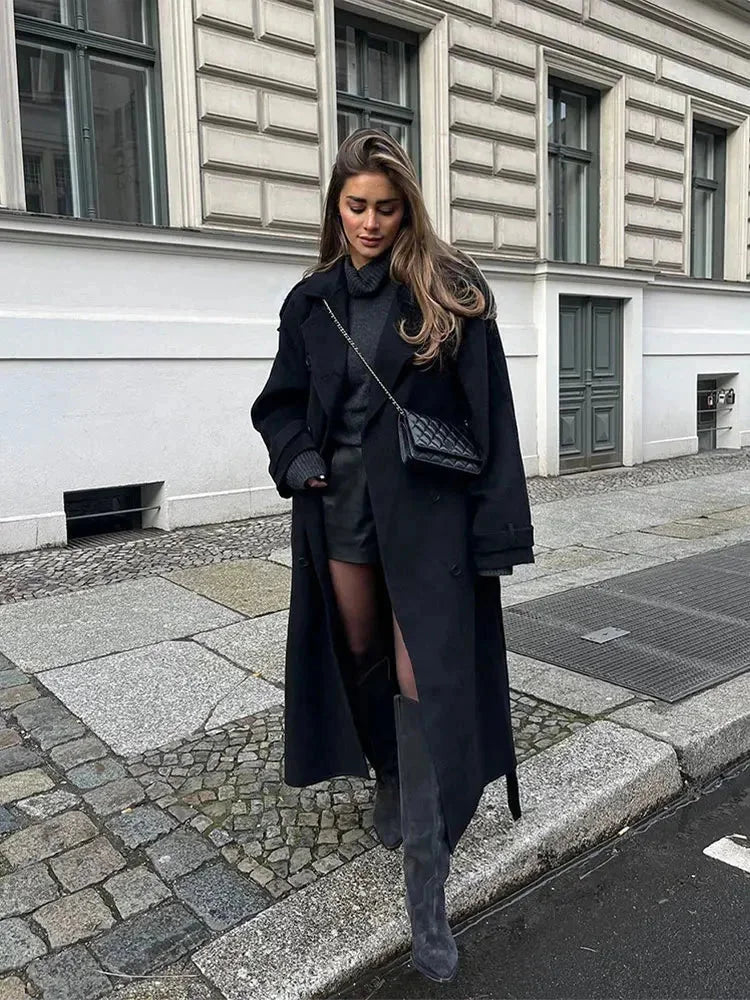 Manteau long noir femme avec ceinture, larges revers et coupe classique, adapté pour les journées froides.