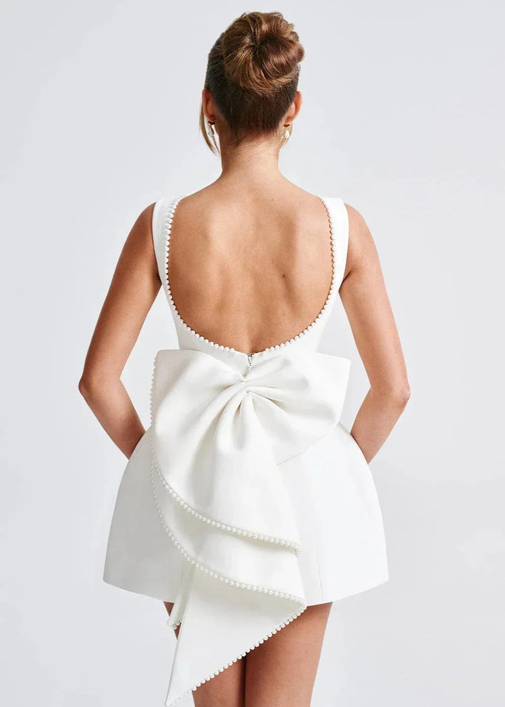 Mini robe dos nu ajustée avec grand nœud, ornée de perles, parfaite pour une soirée élégante. Fabrication douce et…
