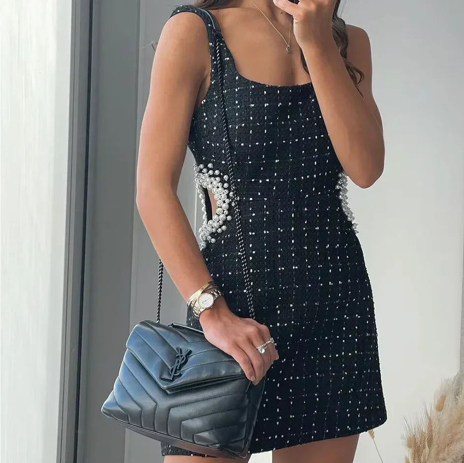Mini robe noire en tissu léger, perlée, avec découpes et manches épaules nues, parfaite pour les soirées et événements.