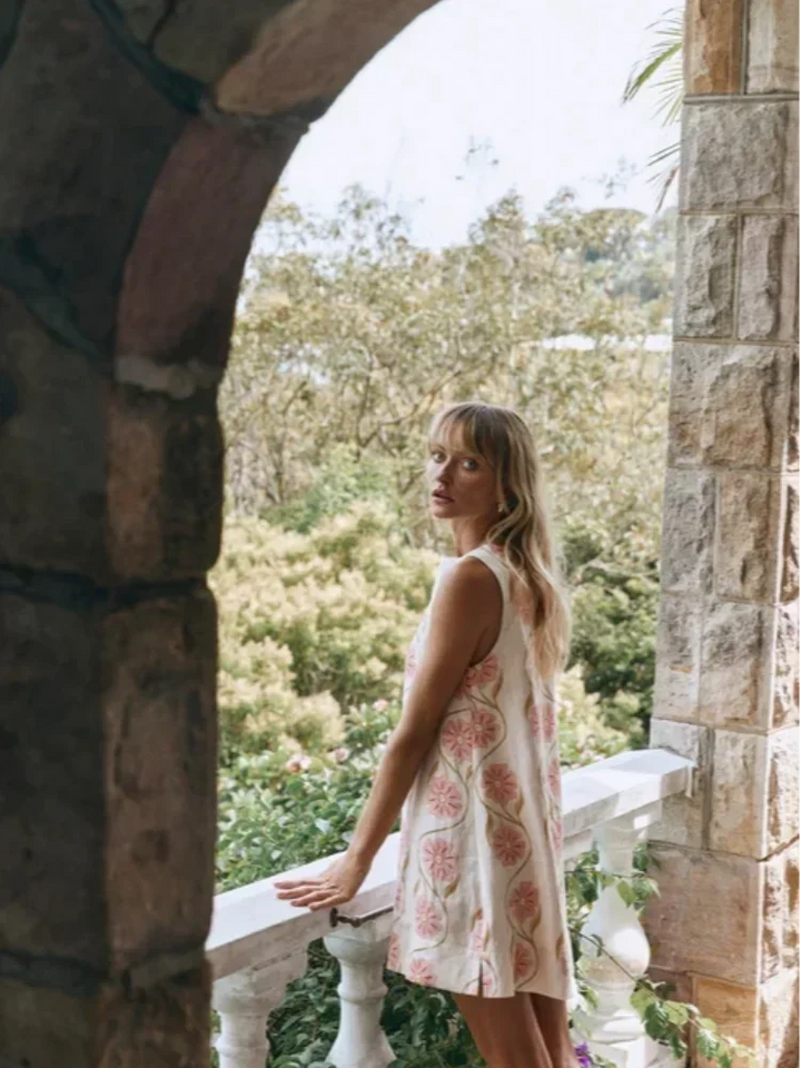 Mini robe sans manches en tissu léger blanc avec un motif de fleurs roses, idéale pour les journées d'été ensoleillées.