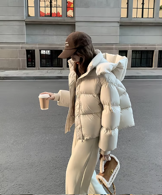 Donna con cappotto imbottito bianco, cappello da baseball marrone, pantaloni beige, tiene caffè e borsa in pelliccia sintetica. Moda invernale urbana.