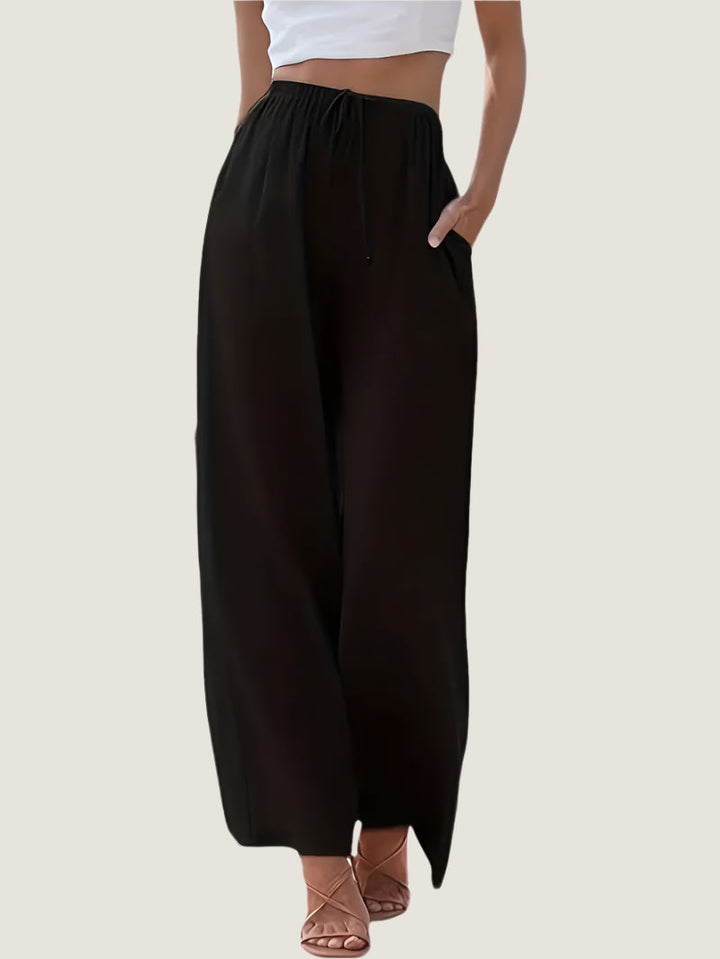 Pantaloni neri larghi da donna, vita alta con coulisse, tasche laterali, abbinati a top bianco corto. Stile casual ed elegante.
