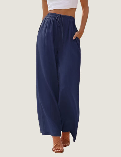 Pantaloni palazzo blu scuro da donna, vita alta con coulisse, tasche laterali, abbinati a top bianco e sandali marroni. Moda estiva casual.