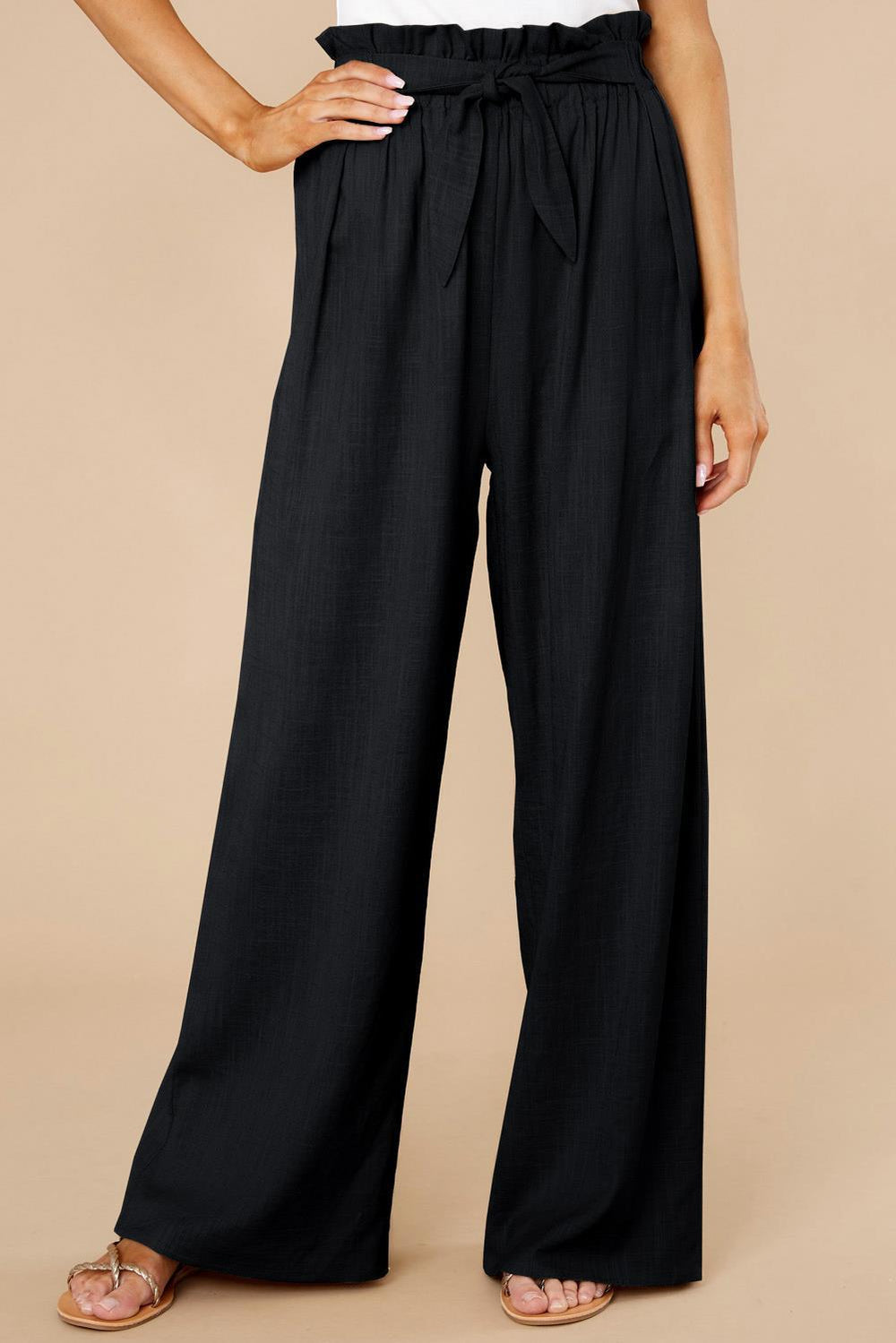 Pantaloni neri a vita alta con cintura, design ampio e pieghe, indossati da una modella. Ideali per look eleganti e casual.