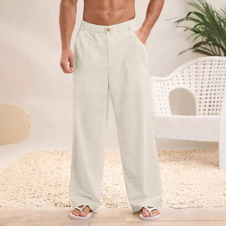 Pantaloni larghi da uomo in lino bianco, stile casual estivo, con tasche laterali. Indossati con sandali bianchi su sfondo neutro.