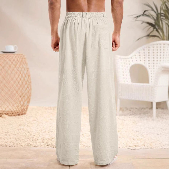 Pantaloni pigiama uomo in cotone bianco, vista posteriore. Design comodo, ideale per relax e notte. Arredo moderno sullo sfondo.