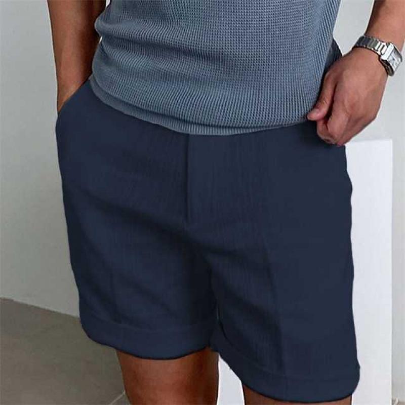 Uomo in pantaloncini blu scuro e maglietta grigia, mani in tasca. Abbigliamento casual estivo, moda maschile, stile moderno.
