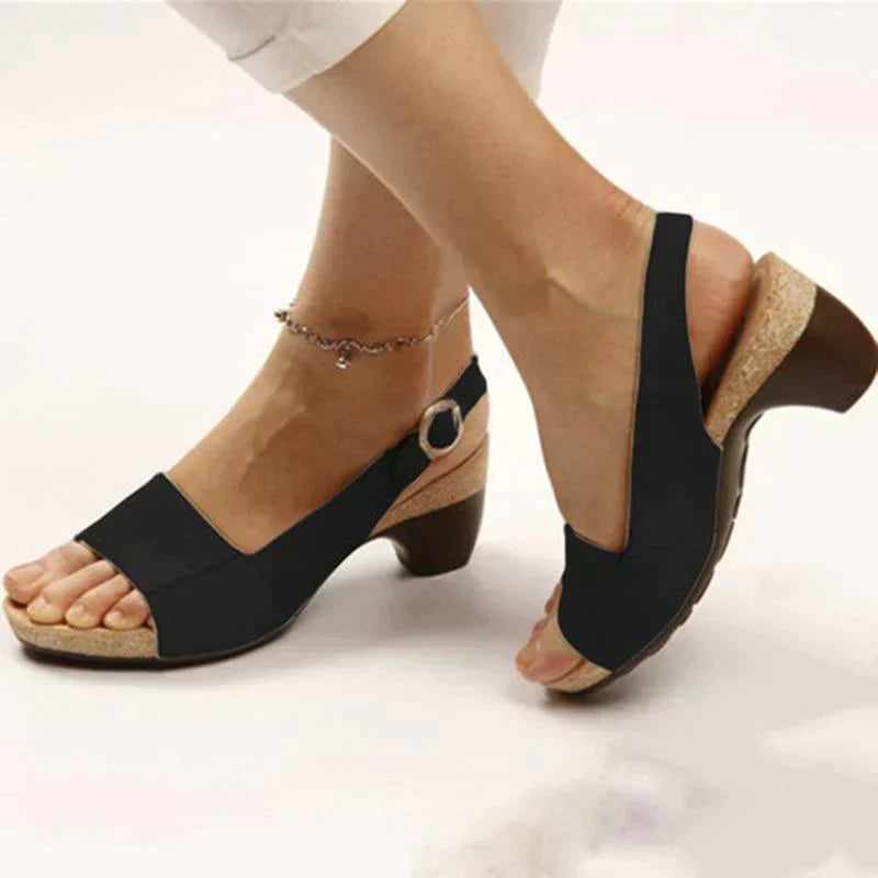 Sandali donna neri con tacco basso, cinturino regolabile, suola in sughero, indossati con pantaloni bianchi. Scarpe estive eleganti e comode.