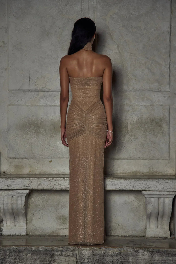 Robe longue beige sans bretelles en tissu scintillant, avec des plis élégants pour une silhouette raffinée.