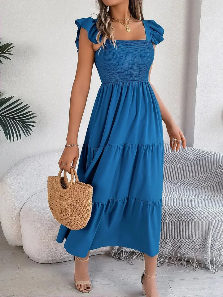 Robe longue smockée bleu avec volants, manches courtes et tissu léger pour un confort optimal. Parfaite pour l'été.