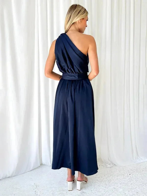 Robe longue femme une épaule en tissu fluide, cintrée à la taille avec une ceinture, parfaite pour les occasions spéciales.