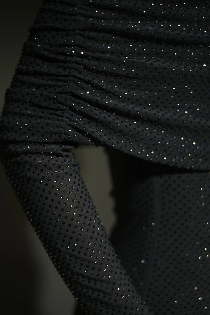 Robe longue longue scintillante avec épaules dénudées, manches longues et détails brillants en tissu léger et fluide.