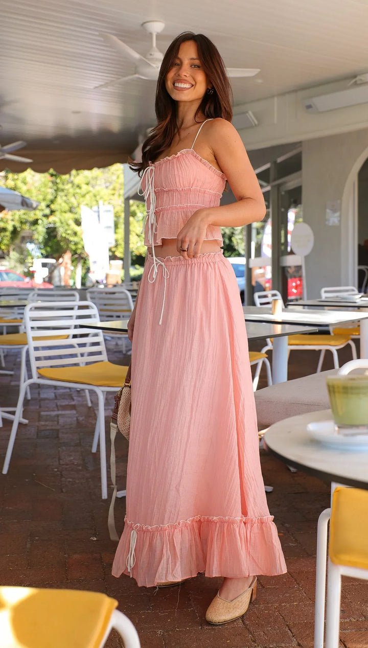 Robe longue rose en tissu léger, avec volants et liens, idéale pour les journées d'été. Design fluide et élégant.