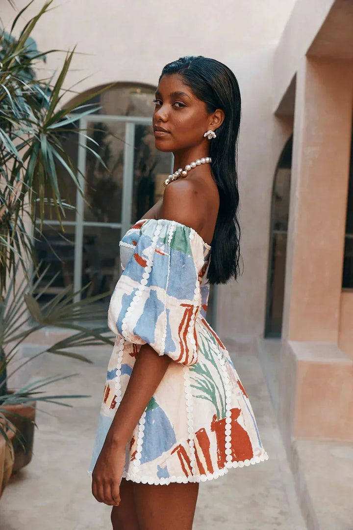 Robe courte blanche à imprimé, manches bouffantes et épaules dénudées, parfaite pour une journée d'été à la plage.