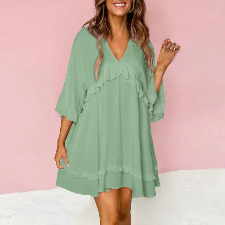Robe courte fluide avec volants, col V et manches larges, en tissu léger, disponible en plusieurs couleurs.