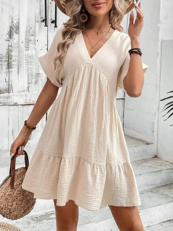 Robe courte fluide avec volants superposés, col V et manches courtes, en tissu léger pour un confort estival. Disponible en…