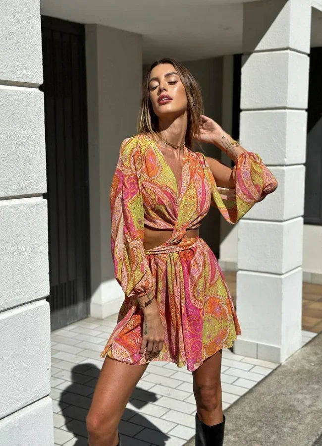 Robe courte imprimée rose et jaune, col V, manches longues, coupe portefeuille fluide idéale pour l'été à la plage.