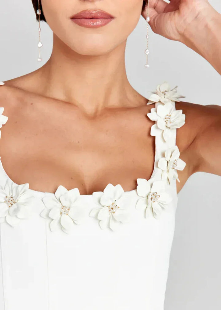 Robe courte noire sans manches ornée de fleurs blanches brodées, idéale pour des soirées élégantes. Fabriquée en tissu léger.