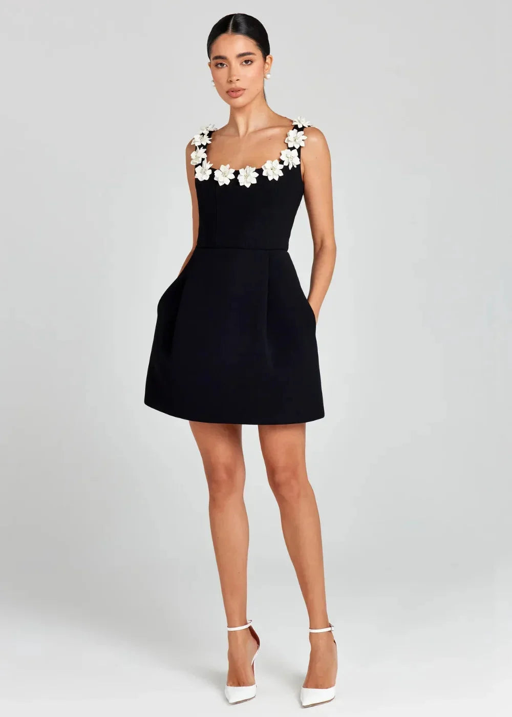 Robe courte noire sans manches, brodée de fleurs blanches, en tissu léger. Parfaite pour une soirée élégante.