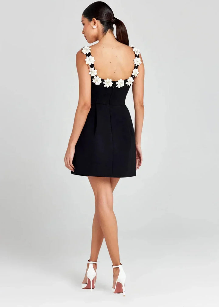 Robe courte noire sans manches, brodée de fleurs blanches, en tissu léger, idéale pour des soirées élégantes.