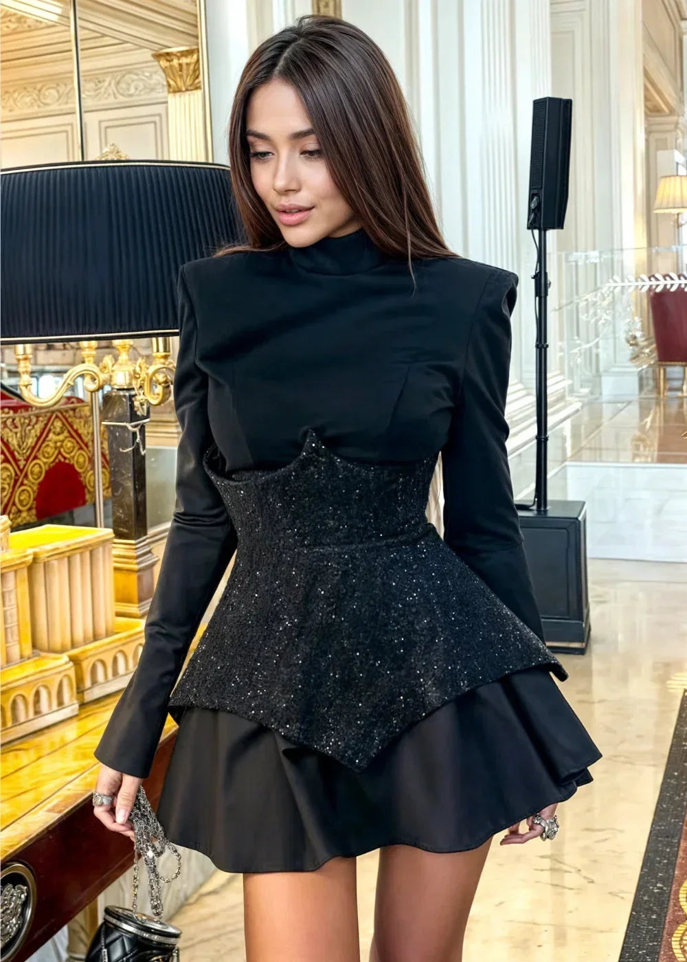 Robe courte noire à peplum en tissu léger, avec sequins brillants et manches longues, idéale pour les soirées élégantes.