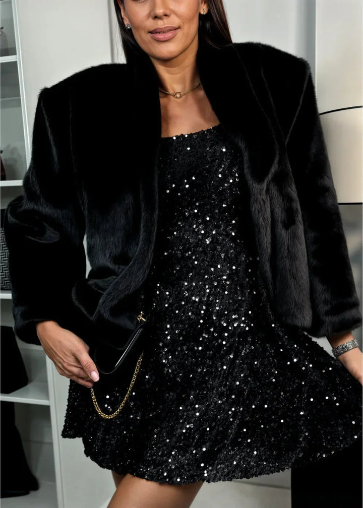 Robe courte noire en paillettes, manches longues, col en cœur, coupe ajustée pour soirées festives. Matière scintillante.