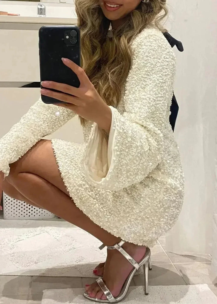 Robe courte blanche à manches longues en tissu brillant, avec un col chic, idéale pour une soirée élégante.