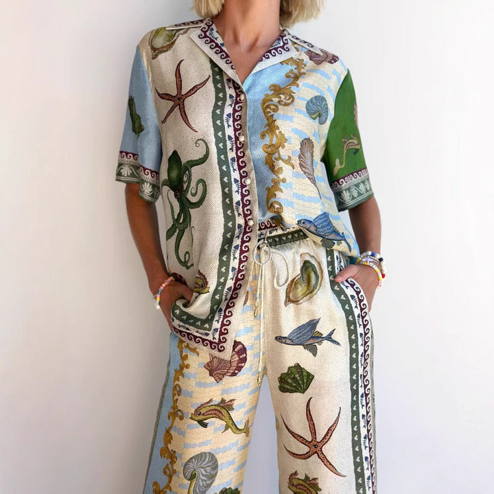 Completo estivo donna con stampa marina, polpo e conchiglie, camicia e pantaloni coordinati, moda casual, sfondo bianco.