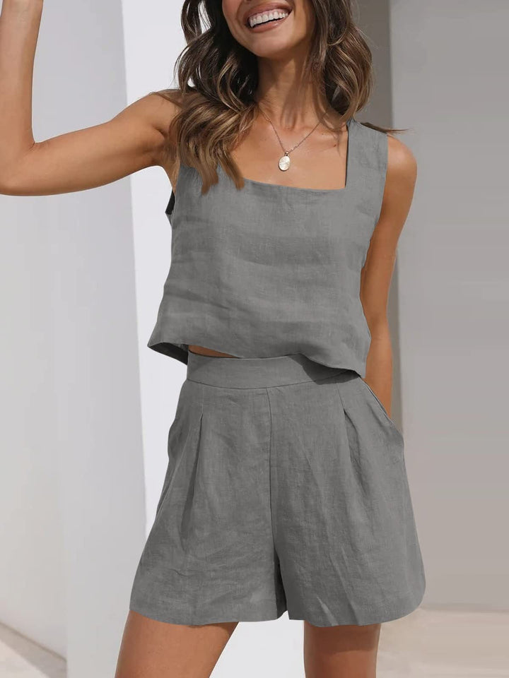 Donna sorridente in completo estivo grigio, top senza maniche e pantaloncini in lino. Moda casual, abbigliamento leggero, stile estivo elegante.