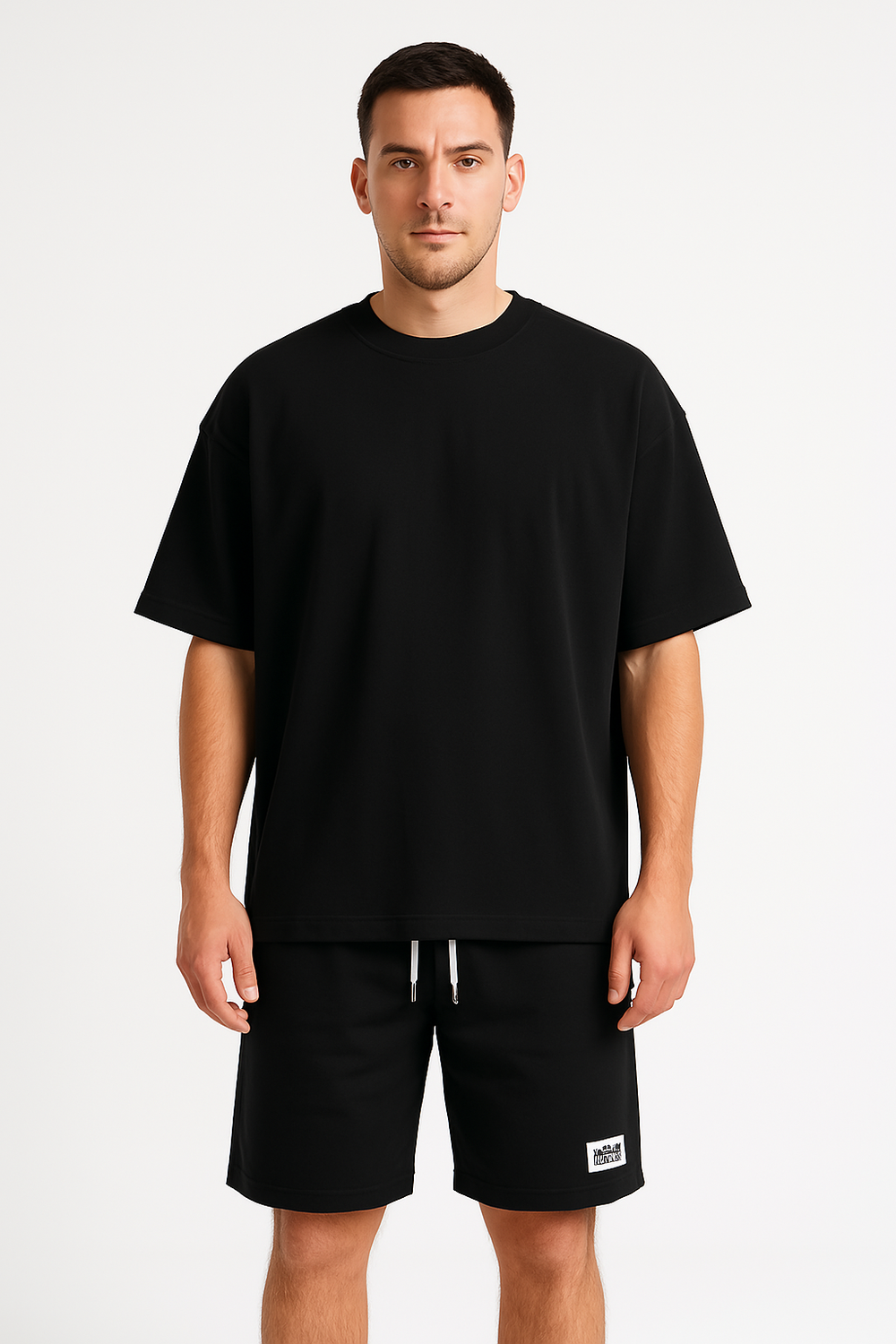 Maglietta nera oversize uomo, abbinata a pantaloncini neri con logo bianco. Abbigliamento casual moderno, moda maschile, stile minimalista.