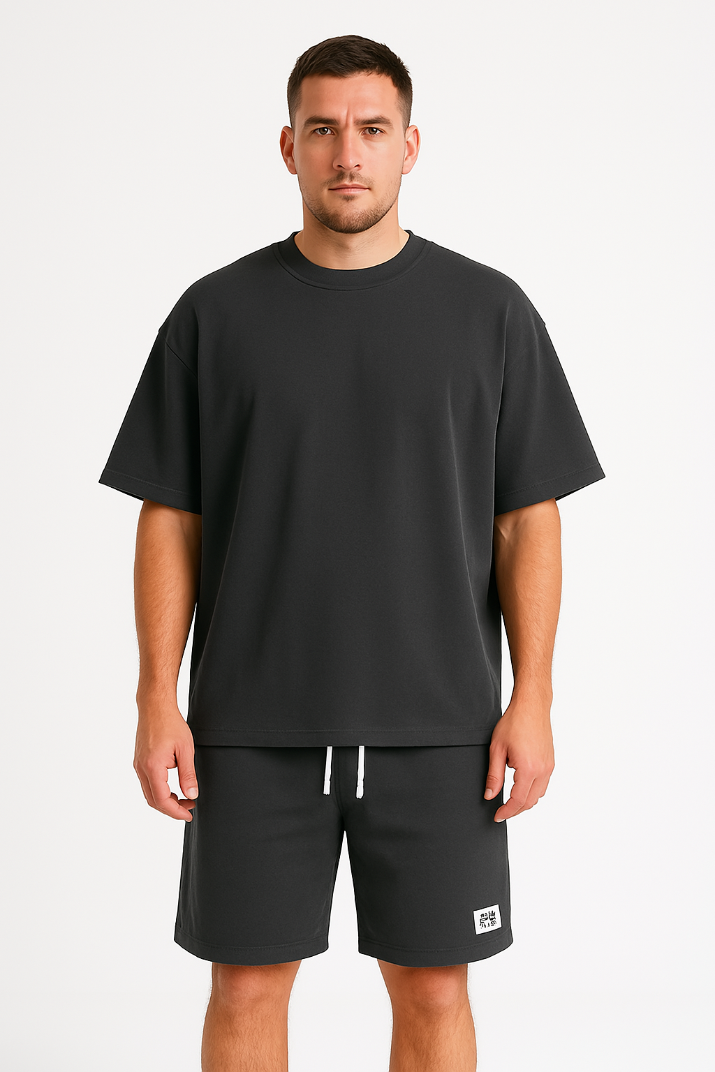 Uomo con t-shirt nera oversize e pantaloncini abbinati, su sfondo bianco. Abbigliamento casual estivo, moda uomo, stile minimalista.