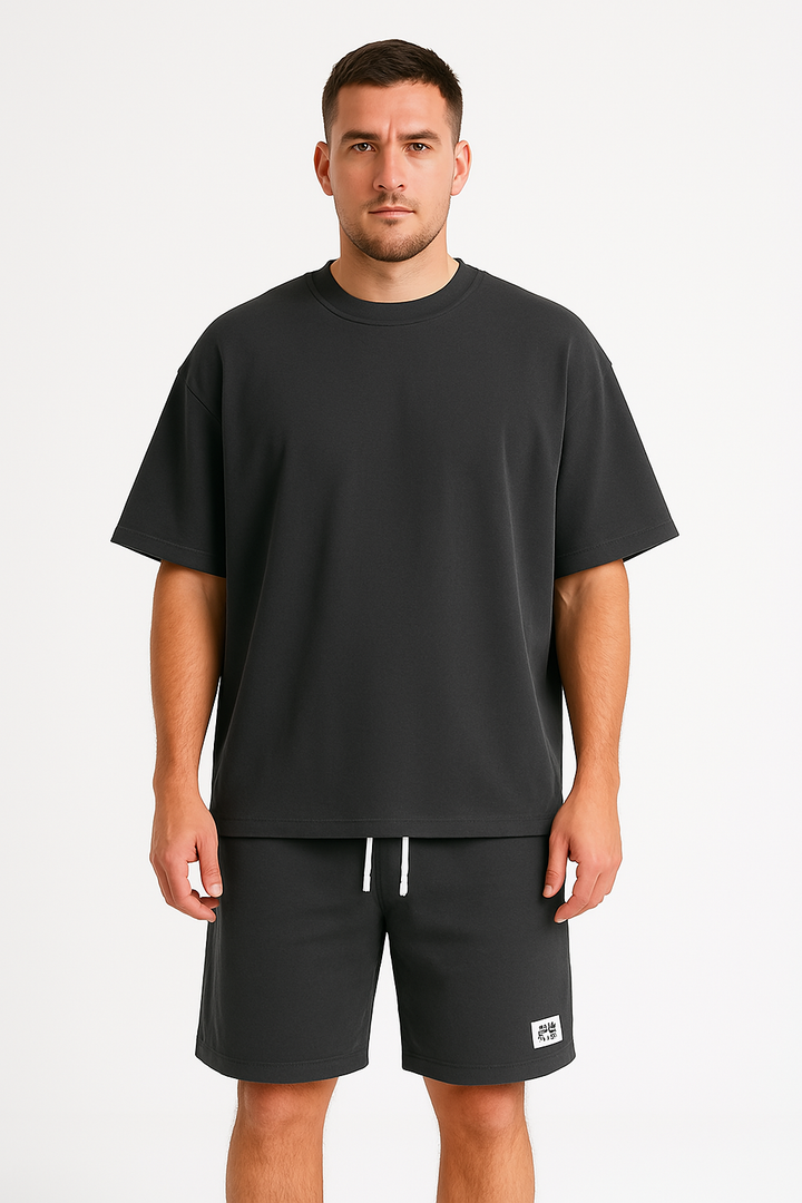 Uomo con t-shirt nera oversize e pantaloncini abbinati, su sfondo bianco. Abbigliamento casual estivo, moda uomo, stile minimalista.