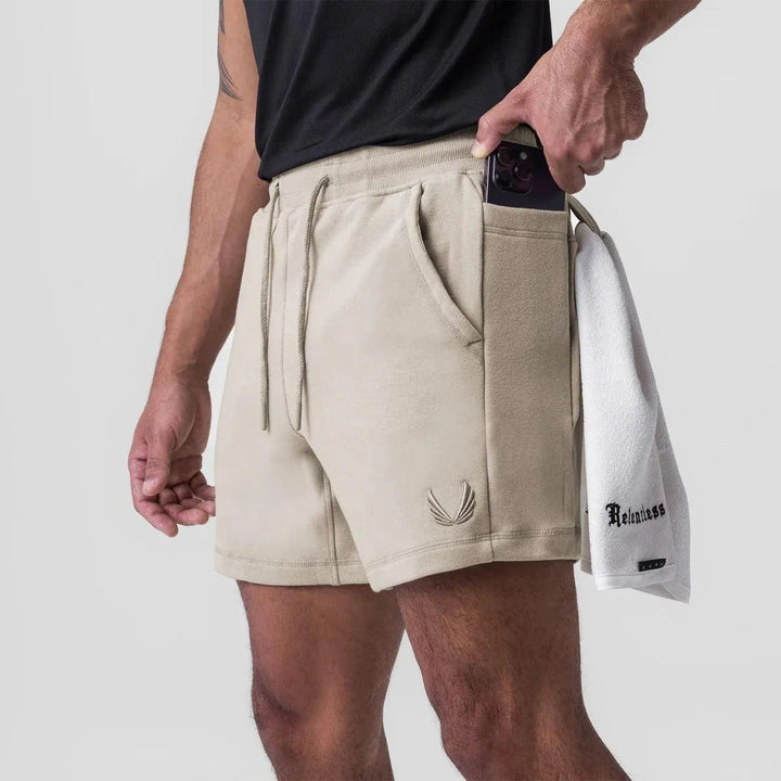 Uomo in pantaloncini beige con tasca per smartphone, asciugamano bianco, maglietta nera. Abbigliamento sportivo estivo, moda casual maschile.