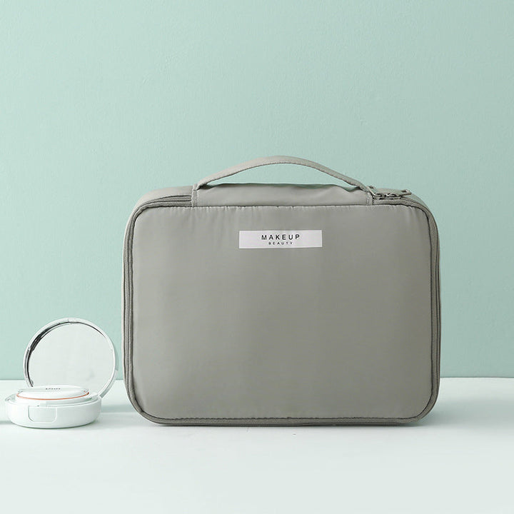 Borsa trucco grigia con manico, design elegante e compatto, ideale per organizzare cosmetici. Include specchio portatile. Perfetta per viaggi.