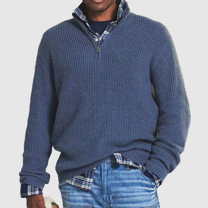 Maglione uomo blu con zip, indossato sopra camicia a quadri, abbinato a jeans. Stile casual, moda autunno-inverno, abbigliamento maschile.