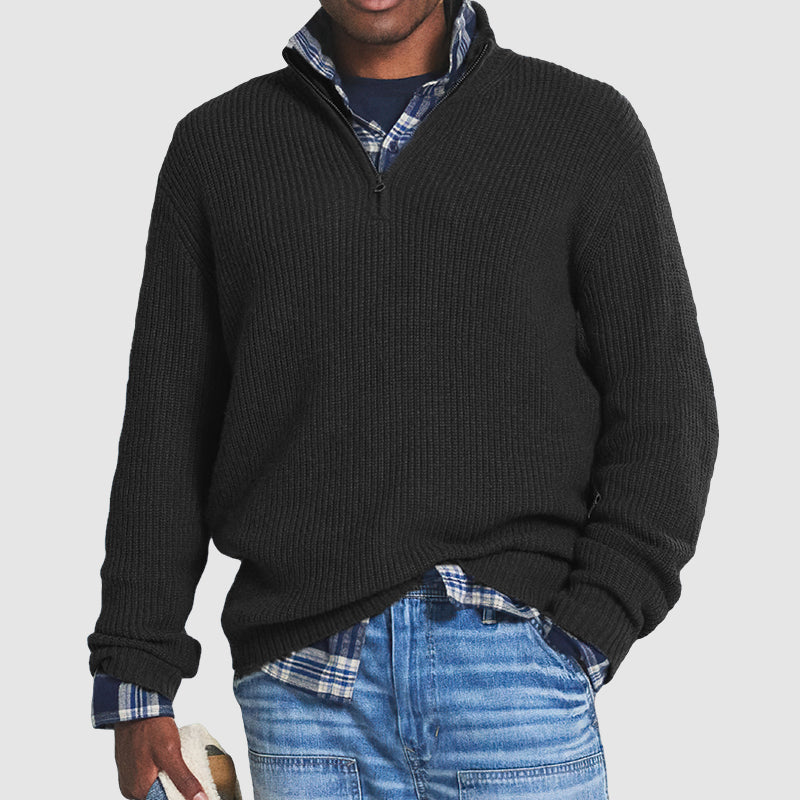 Maglione nero a collo alto con zip, indossato sopra camicia a quadri blu e jeans. Look casual maschile, moda autunno inverno.