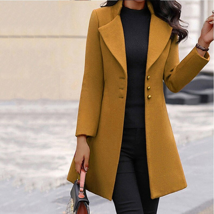 Cappotto lungo donna giallo senape, elegante, con bottoni, abbinato a maglia nera e pantaloni scuri. Moda autunnale, stile sofisticato.