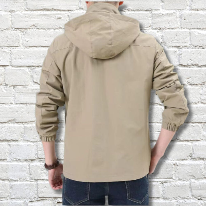 Giacca a vento beige da uomo con cappuccio, vista posteriore, su sfondo di mattoni bianchi. Moda casual, abbigliamento esterno leggero.
