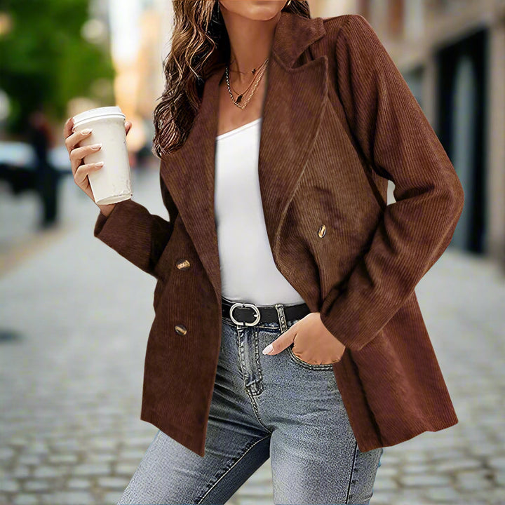 Giacca marrone a coste su donna con caffè in mano, jeans e cintura nera. Moda autunnale casual in strada urbana.