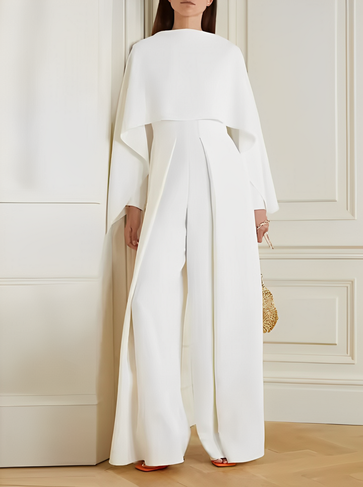 Tuta elegante bianca da donna con mantella, design moderno, indossata in interni. Perfetta per eventi formali e cerimonie.