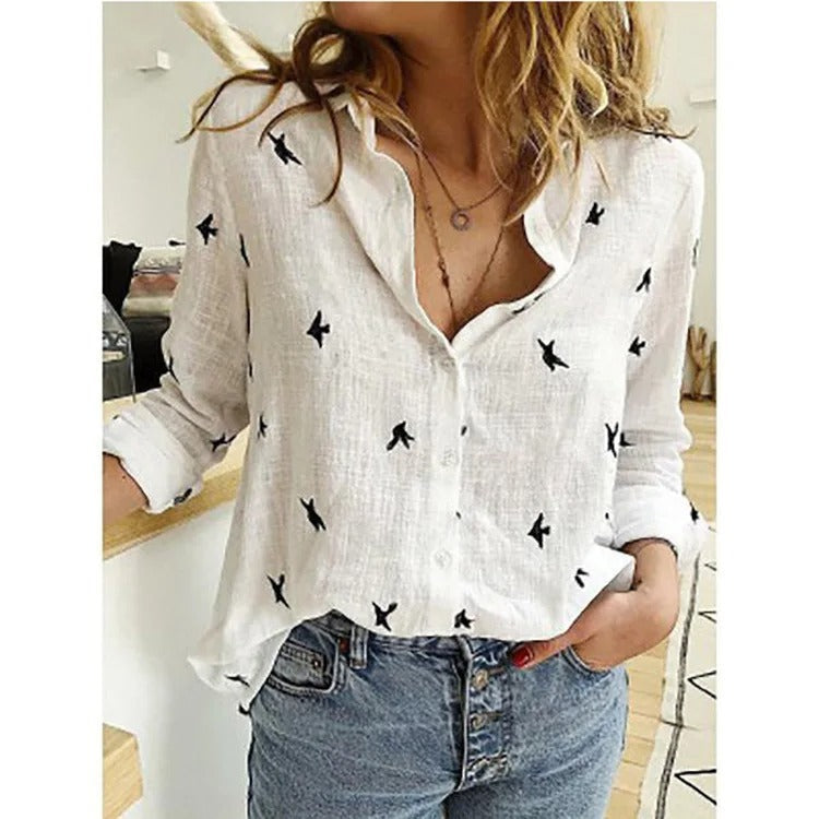 Camicia bianca in lino con motivo a uccelli neri, maniche lunghe arrotolate, abbinata a jeans a vita alta. Stile casual e moderno per donna.
