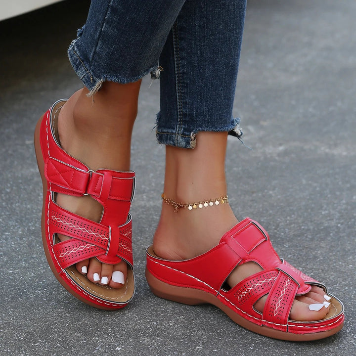 Sandali rossi da donna in pelle, con cinturino regolabile e suola comoda, indossati con jeans strappati. Scarpe estive eleganti e casual.