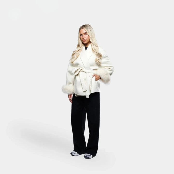 Veste blanche pour femme, ceinturée, avec manches en fourrure synthétique et coupe ajustée.
