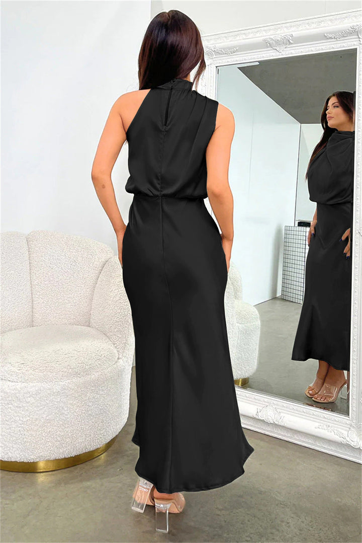 Abito lungo nero elegante, senza maniche, con schiena scoperta. Donna riflessa in uno specchio, indossa tacchi trasparenti. Arredamento moderno.