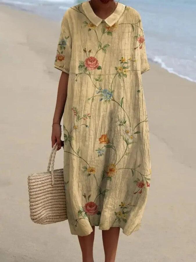 Abito estivo lungo floreale in lino, maniche corte, colletto a camicia, indossato su spiaggia. Borsa di paglia intrecciata. Moda donna casual.